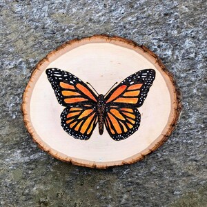 May include: A wooden round slice with a painted monarch butterfly in orange, black, and white.