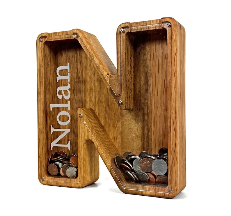 Wooden Piggy Bank Letter N with Personalized Name Engraved on the Clear Front With a White Background. Made with USA Red Oak, natural wood gives a brown reddish look