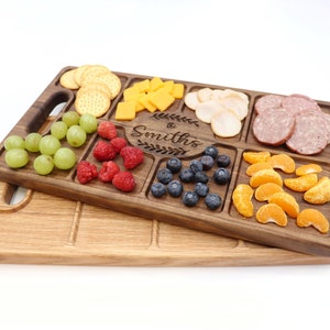 Walnut wood charcuterie board Sitting on top of a Red Oak Charcuterie with a white background 
With
Blueberries, raspberries, Oranges, Ham and Cheese spread out on top
