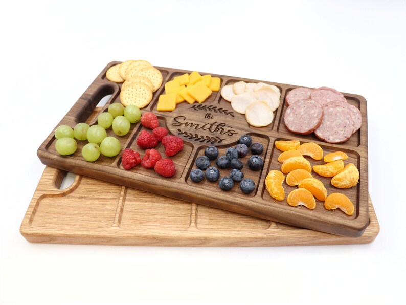 Walnut wood charcuterie board Sitting on top of a Red Oak Charcuterie with a white background 
With
Blueberries, raspberries, Oranges, Ham and Cheese spread out on top