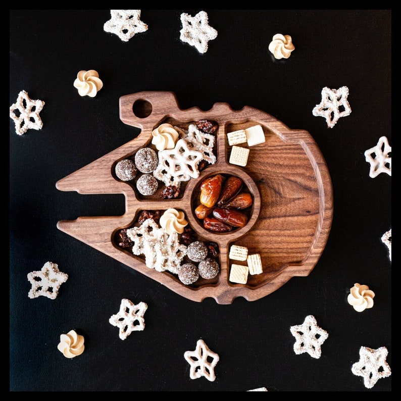 Wooden Tray shaped like a Millennium Falcon, sitting on a black background surrounded by Pretzels. The tray has 5 compartments