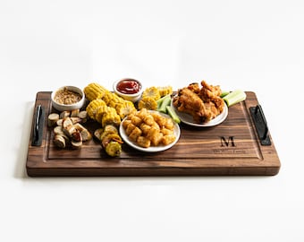 May include: A wooden serving board with handles, personalized with the letter "M" and the text "The Miller Family". The board is filled with various snacks, including corn on the cob, chicken wings, tater tots, sausage, pickles, mustard, and ketchup.