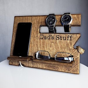 May include: A wooden organizer with the text "Dad's Stuff" engraved on it. It has slots for two watches, a phone stand, and a shelf for glasses.