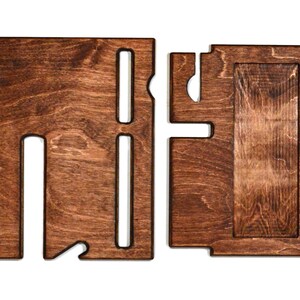 May include: A wooden phone stand with two slots for phones and a separate compartment for charging cables. The stand is made of dark brown wood and has a natural wood grain.
