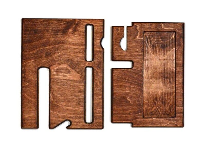 May include: A wooden phone stand with two slots for phones and a separate compartment for charging cables. The stand is made of dark brown wood and has a natural wood grain.