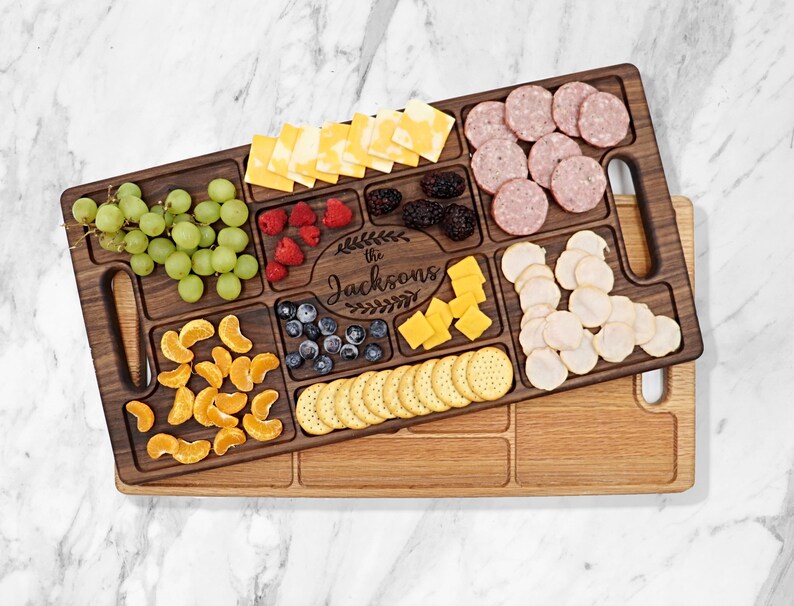 Walnut wood charcuterie board Sitting on top of a Red Oak Charcuterie with a white background 
With
Blueberries, raspberries, Oranges, Ham and Cheese spread out on top