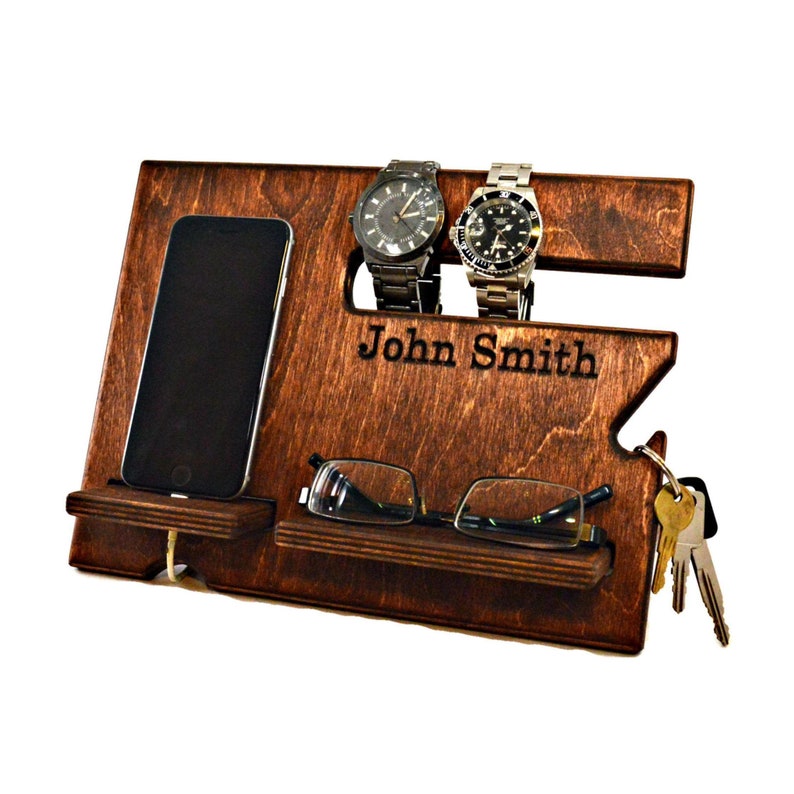 May include: A dark brown wooden organizer with slots for watches, a phone, glasses, and keys. The organizer has the name "John Smith" engraved on the front.