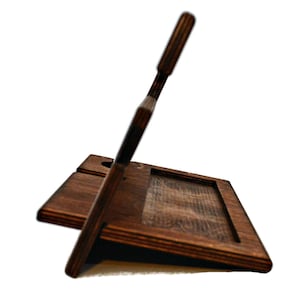 May include: A dark brown wooden phone stand with a slot for charging cables. The stand has a raised back to prop up a phone or tablet.