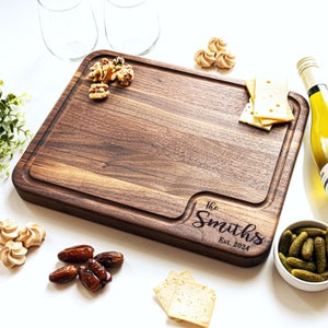 May include: A large, rectangular wooden cutting board with a natural wood grain finish. The board has a raised edge and a carved design in the lower right corner that reads "The Smiths Est. 2024".