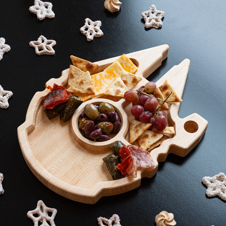 Wooden Millennium Falcon Shaped Tray with 5 compartments with appetizers in each one. Wood is light and sitting on a black backdrop.