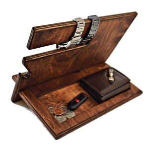 May include: A wooden organizer with a brown stain finish. It has a slot for watches, a compartment for a wallet, and a small area for loose items like keys or coins.