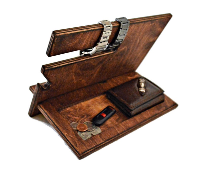 May include: A wooden organizer with a brown stain finish. It has a slot for watches, a compartment for a wallet, and a small area for loose items like keys or coins.