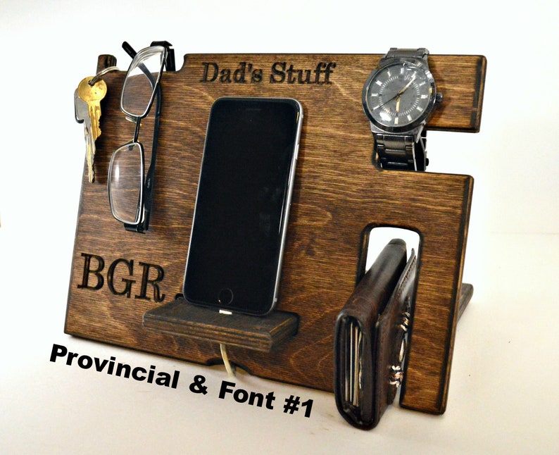 Może przedstawiać: Drewniany organizer z miejscami na telefon, zegarek, klucze i portfel. Organizer jest grawerowany tekstem "Dad's Stuff" i "BGR".