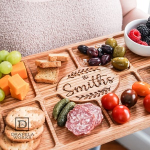 Someone holding a Red Oak Charcuterie Board with Fruit, Ham, Crackers and Cheese on top of the charcuterie