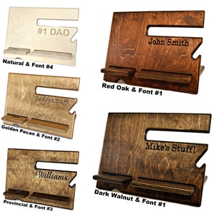 May include: Four wooden phone stands with different wood finishes and engraved text. The stands have two shelves for holding phones and other items. The wood finishes are natural, red oak, golden pecan, and dark walnut. The engraved text includes "#1 DAD", "John Smith", "Daddy's Stuff", "Mike's Stuff!", and "Williams".