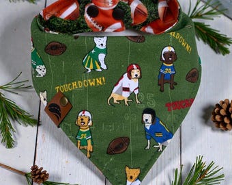 May include: Green dog bandana with a football theme. The bandana features illustrations of dogs in football uniforms, footballs, and the words "Touchdown!" and "Touchdown". The reverse side has a football field pattern.