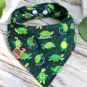 May include: A green bandana with a pattern of turtles riding scooters and skateboards. The bandana has two white snaps on the back.