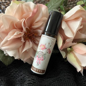 May include: A small glass bottle with a black rollerball top. The bottle is labelled with a floral design and the word "COSETTE".