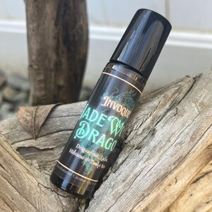 May include: A black roller bottle with a green and gold label that says "INVOGUE JADE W/ DRAGO Dragon fruit, Lychee, Hibiscus & Tonka Via Fractionated Coconut Oil 10 ml"