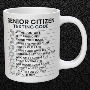 Puede incluir: Taza de cerámica blanca con un diseño negro que dice "Senior Citizen Texting Code" y enumera abreviaturas comunes de mensajes de texto y sus significados.