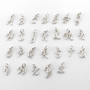 May include: A collection of silver-colored alphabet charms, each in a different cursive font. The charms are small, with a loop at the top for attaching to a necklace or bracelet. The letters A through Z are displayed.