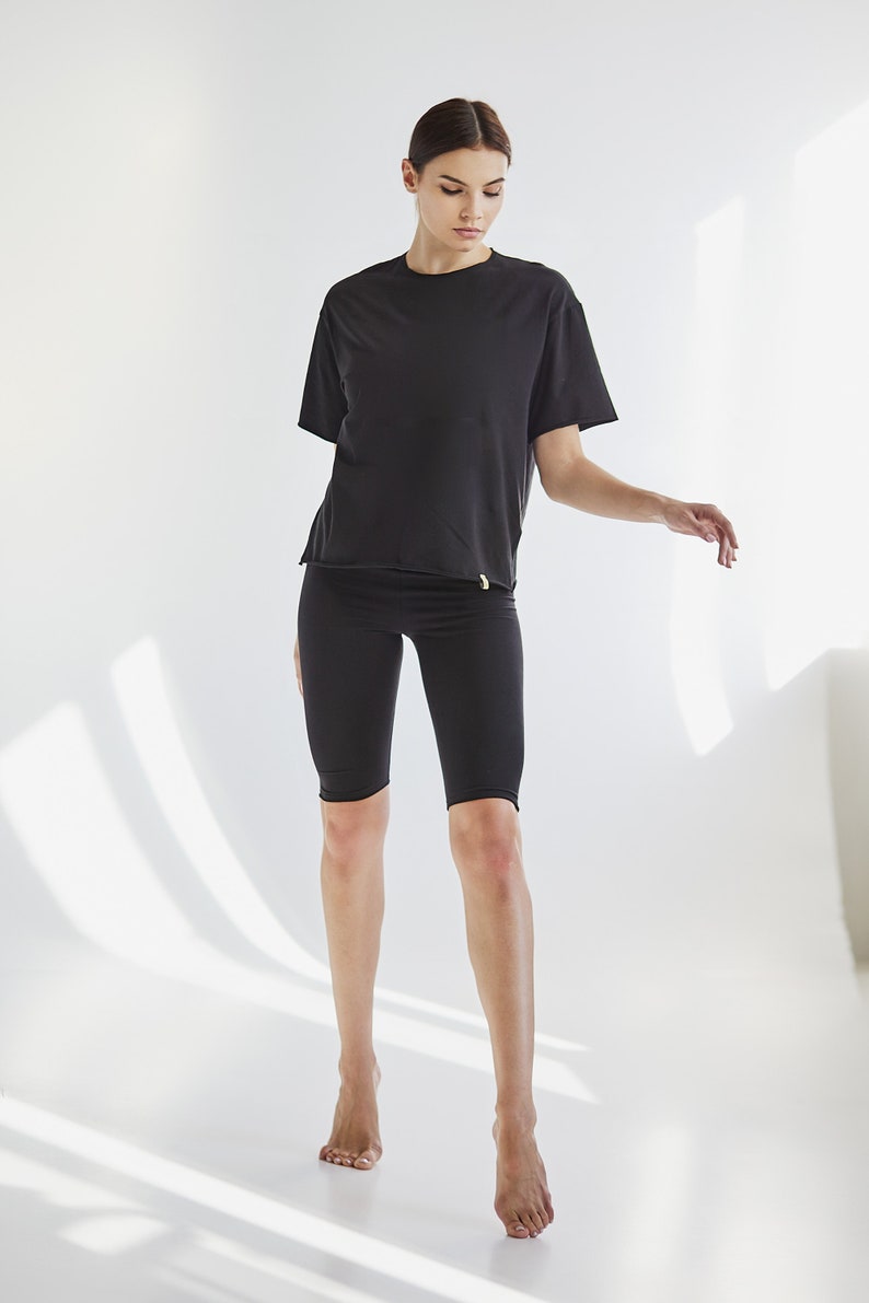 K&ouml;nnte beinhalten: Eine Frau tr&auml;gt ein schwarzes T-Shirt mit kurzen &Auml;rmeln und schwarze Radlerhosen. Sie steht auf einem wei&szlig;en Hintergrund.
