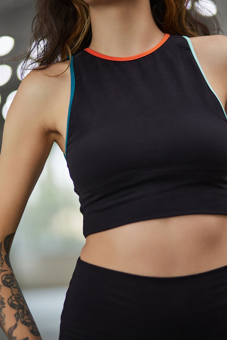May include: A black athletic crop top with a teal and orange trim. The top is sleeveless and has a high neckline.