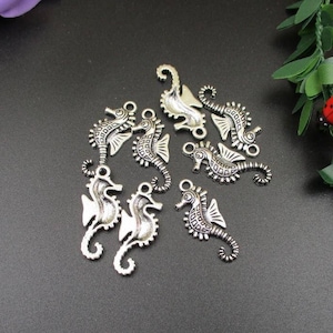 Könnte beinhalten: Eine Sammlung von acht silberfarbenen Seepferdchen-Anhängern mit filigranen Details. Die Anhänger eignen sich perfekt für die Schmuckherstellung, das Scrapbooking oder andere Bastelprojekte.