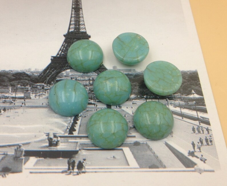 May include: Seven turquoise cabochon stones with a marbled pattern. The stones are round and have a smooth, polished surface.