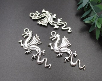 May include: Three silver dragon charms with intricate details. The dragons are in various poses, with wings and tails. The charms are perfect for jewelry making or crafting.