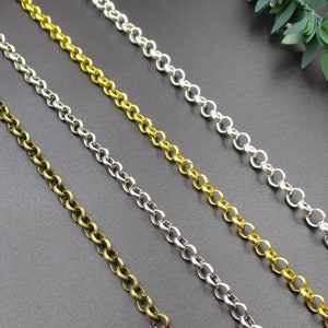 May include: Close-up of four metal chain strands in bronze, silver, and gold tones. The chains are made of small, round links, and are arranged diagonally across a dark surface. Decorative elements.