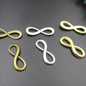 May include: Six infinity symbol charms in gold, silver, and bronze finishes. The charms are all the same size and shape, and they are arranged in a random pattern on a black surface.