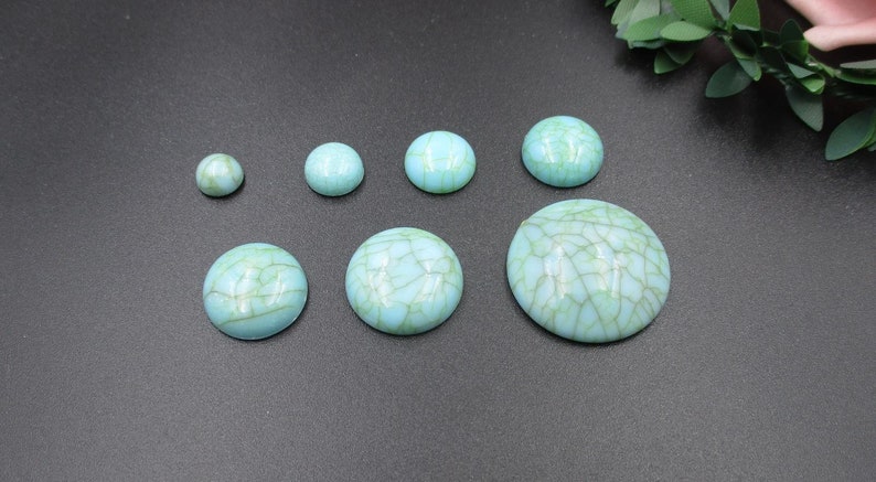 May include: Assortment of turquoise cabochons in various sizes. The cabochons have a marbled pattern with a light blue base and green veins.