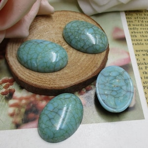 May include: Four oval-shaped turquoise cabochons with a crackled finish. The cabochons are on a wooden surface.