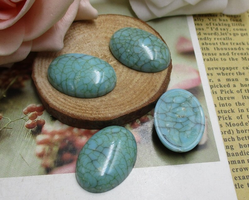 May include: Four oval-shaped turquoise cabochons with a crackled finish. The cabochons are on a wooden surface.