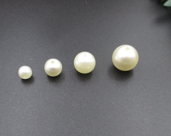May include: Five white pearl beads of varying sizes, arranged in a row from smallest to largest on a black surface.