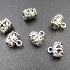Puede incluir: Seis tapones de cuentas de metal plateados con un diseño floral. Cada tapón tiene un pequeño bucle para sujetarlo a una cuerda o cordón.