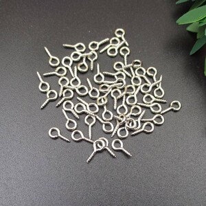 May include: A large quantity of silver-toned eyelet screw-back findings. These are small, round metal loops with a screw-on back, used for attaching jewelry or other crafts.