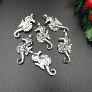 Könnte beinhalten: Sechs silberfarbene Seepferdchen-Anhänger mit filigranen Details. Die Anhänger eignen sich perfekt für die Schmuckherstellung oder Bastelprojekte.