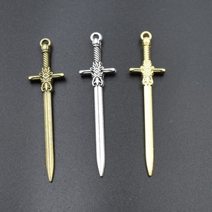 May include: Three ornate sword charms in different finishes: gold, silver, and bronze. Each charm features a detailed cross-shaped hilt and a pointed blade.