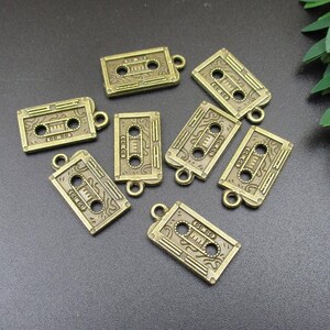 Puede incluir: Una colecci&oacute;n de ocho abalorios de metal de color dorado antiguo con forma de cintas de casete. Cada abalorio tiene un dise&ntilde;o detallado y un bucle para sujetarlo a un collar, pulsera o llavero.