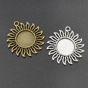 Può includere: Due vassoi pendenti in metallo a forma di sole, uno dorato e uno argentato, con un centro rotondo aperto per aggiungere un cammeo o altri abbellimenti.