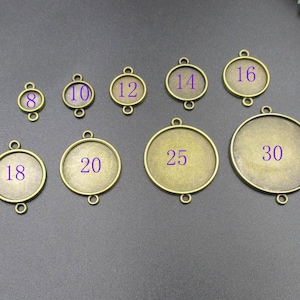 Peut inclure: Une collection de plateaux de lunette de couleur bronze antique de différentes tailles, allant de 8 à 30. Chaque plateau a un design circulaire avec deux boucles pour l'attacher à une chaîne ou à un autre composant de bijou. Les chiffres sont violets.