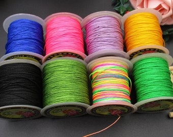 Könnte beinhalten: Acht Spulen mit farbigem geflochtenem Kordel, jede um eine weiße Kunststoffspule mit einem schwarzen Etikett gewickelt. Die Farben sind Schwarz, Grün, Pink, Lila, Gelb, Blau, Regenbogen und Neon-Grün.