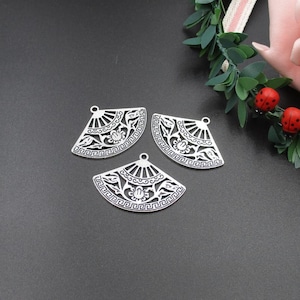 Könnte beinhalten: Drei silberne Metall-Anhänger in Fächerform mit filigranen Blumendesigns. Die Anhänger haben ein ausgeschnittenes Design und sind perfekt für die Schmuckherstellung oder das Basteln.