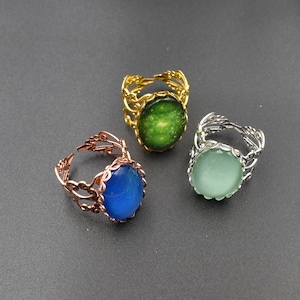 Può includere: Tre anelli ornati con pietre ovali. Uno è dorato con una pietra verde, un altro è ramato con una pietra blu, e il terzo è argentato con una pietra verde chiaro. Gli anelli hanno un design traforato e decorativo.