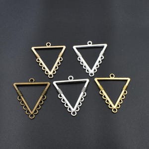 May include: Five triangle-shaped metal pendant blanks with a decorative edge. The blanks are in silver and gold tones.
