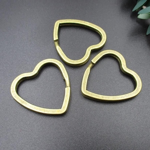 May include: Three gold-colored heart-shaped keychains. The keychains are made of metal and have a smooth finish.