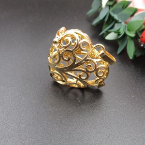 Puede incluir: Un colgante de corazón de color dorado con un delicado diseño de filigrana intrincado. El colgante tiene un bucle en la parte superior para sujetarlo a una cadena o cordón.