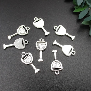 Könnte beinhalten: Ein Set mit zehn silberfarbenen Metall-Anhängern in Form von Weingläsern. Die Anhänger haben eine glitzernde Oberfläche und sind perfekt, um Schmuck oder Bastelarbeiten einen Hauch von Eleganz zu verleihen.